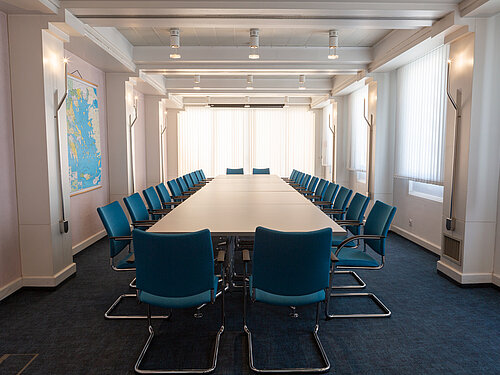 [Translate to Englisch:] Konferenzsaal Deutsche Botschaft Athen, langer Tisch mit blauen Stühlen und Teppich